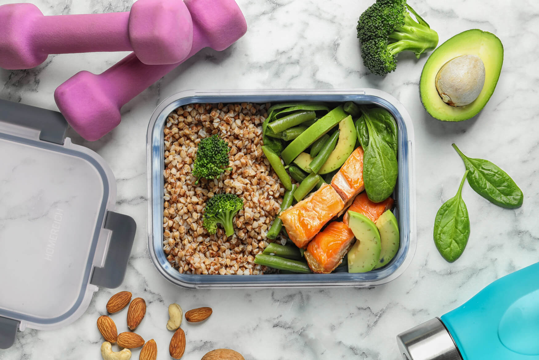 Hochwertige Produktfotografie einer Lunchbox mit gesundem Essen auf Marmor, neben frischer Avocado und Hanteln. Perfekt für die Darstellung von gesunden Lebensmitteln und Lifestyle-Produkten. Authentische Aufnahme für Ihre Markenfotografie und Produktpräsentation.