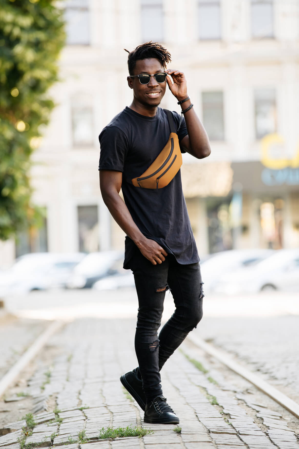 Ein ansprechendes Foto zeigt einen Mann mit einer leuchtend orangefarbenen Hipbag, der gelassen durch eine ruhige Innenstadtstraße schlendert. Die Szene vermittelt Gelassenheit und Urbanität, wobei die Hipbag als modisches Statement im Mittelpunkt steht. Der Kontrast zwischen der Stille der Straße und dem lebendigen Farbtupfer der Tasche fängt die Essenz des urbanen Lebens ein, während der Mann die Ruhe und Schönheit der Stadt genießt.