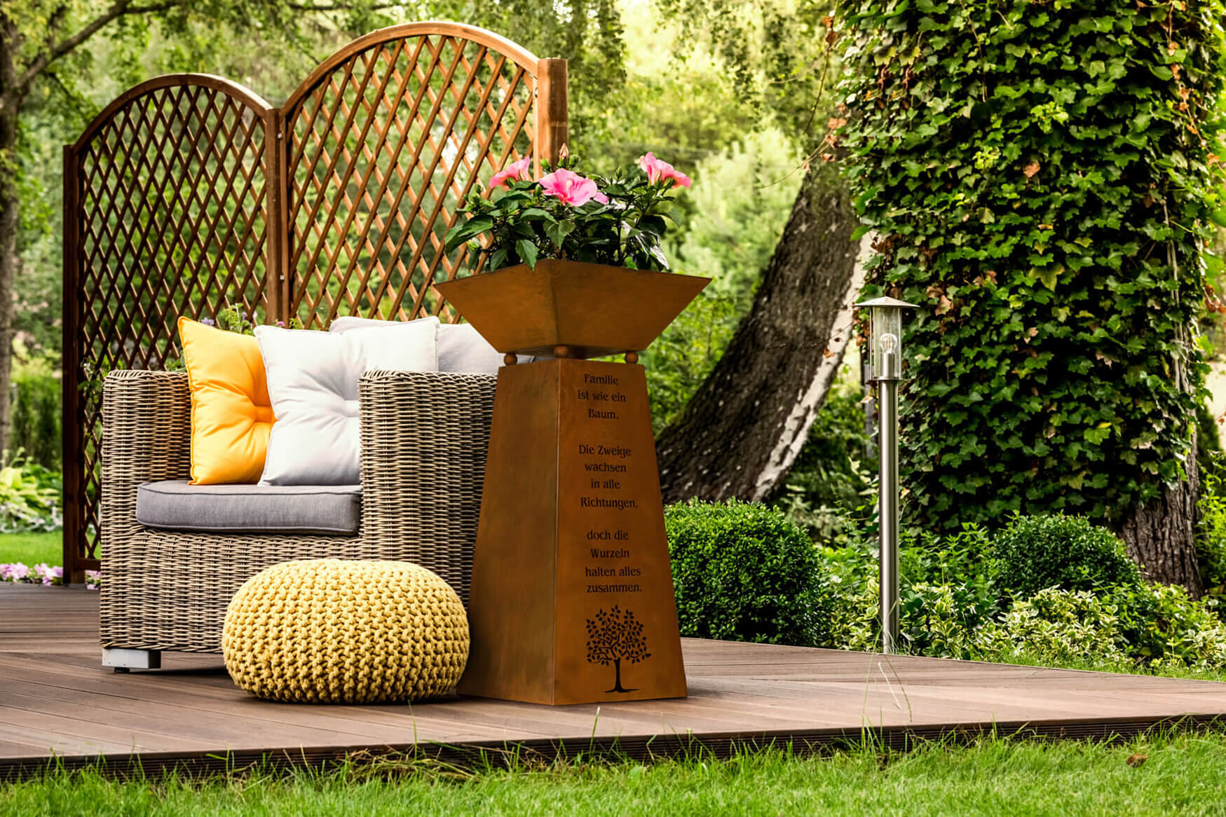 Ein bezauberndes Lifestyle-Werbefoto einer mit frischen Blumen bepflanzten Rost-Blumensäule, die eine malerische Dekoration auf einer Terrasse bildet. Unsere Produktfotografie zeigt die natürliche Schönheit und den Charme dieser liebevoll gestalteten Blumensäule, die jeden Außenbereich in ein blühendes Paradies verwandelt