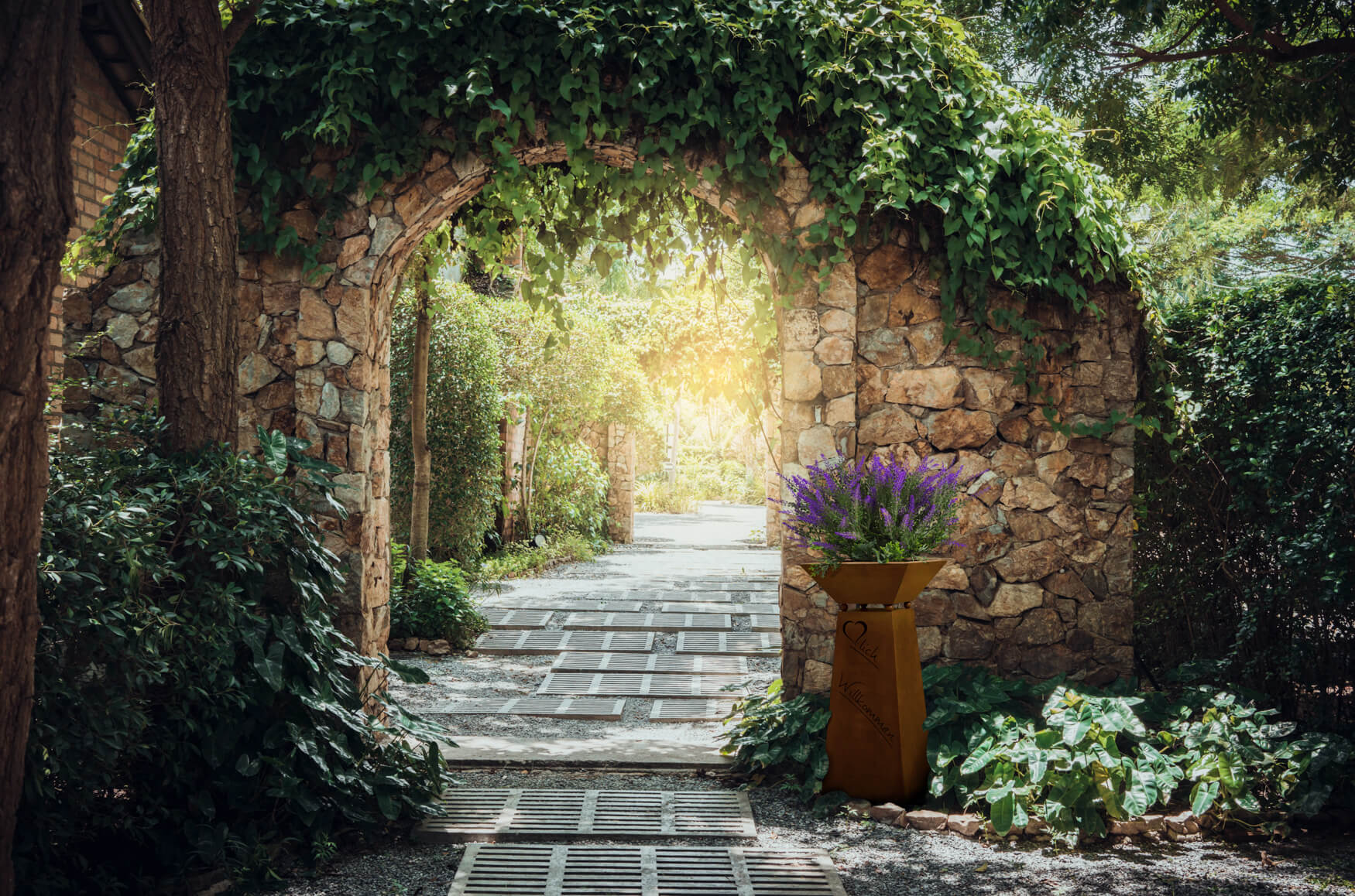 Rostige Blumensäule mit Lavendel vor einem Gartentorbogen.