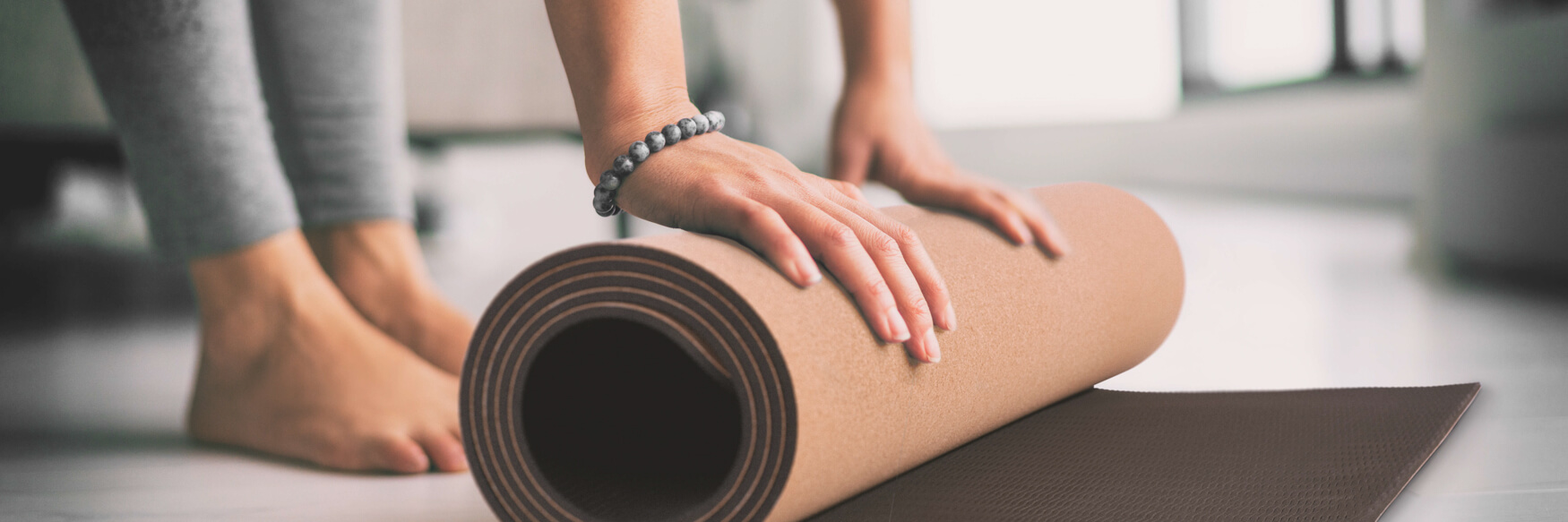 Eine Frau rollt ihre Yogamatte zusammen, nachdem sie ihre Yoga-Session beendet hat. Diese einfache Handlung symbolisiert das Ende einer beruhigenden und revitalisierenden Übung und den Übergang zu einem friedlichen Zustand des Geistes.