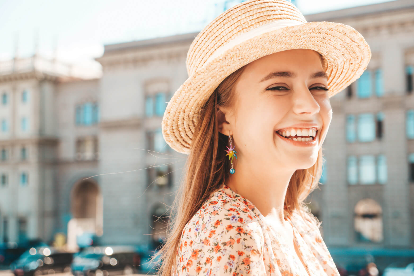 Eine junge Frau mit einem blumigen Kleid und einem Sonnenhut trägt stilvoll farbenfrohe Glasohrringe in einer lebendigen städtischen Umgebung. Diese Szene vereint urbanen Chic mit einem Hauch von Natürlichkeit und versprüht Lebensfreude und Stilbewusstsein. Ein Bild, das die Fantasie anregt und das Verlangen nach dem Produkt weckt, um den persönlichen Stil zu unterstreichen und das Outfit zu vervollständigen